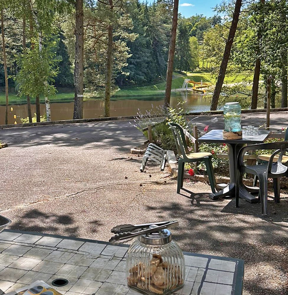 Espace d’accueil extérieur au Domaine du Lac de Soursac avec boissons, guides touristiques et vue sur le lac en pleine nature